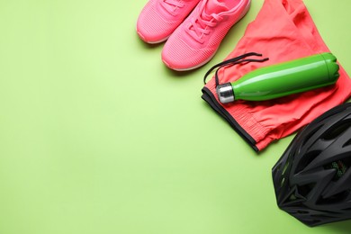 Photo of Flat lay composition with different cycling accessories and clothes on green background, space for text