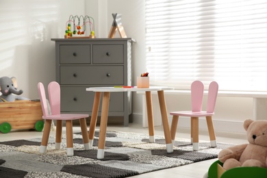Photo of Little table and chairs with bunny ears in children's room. Interior design