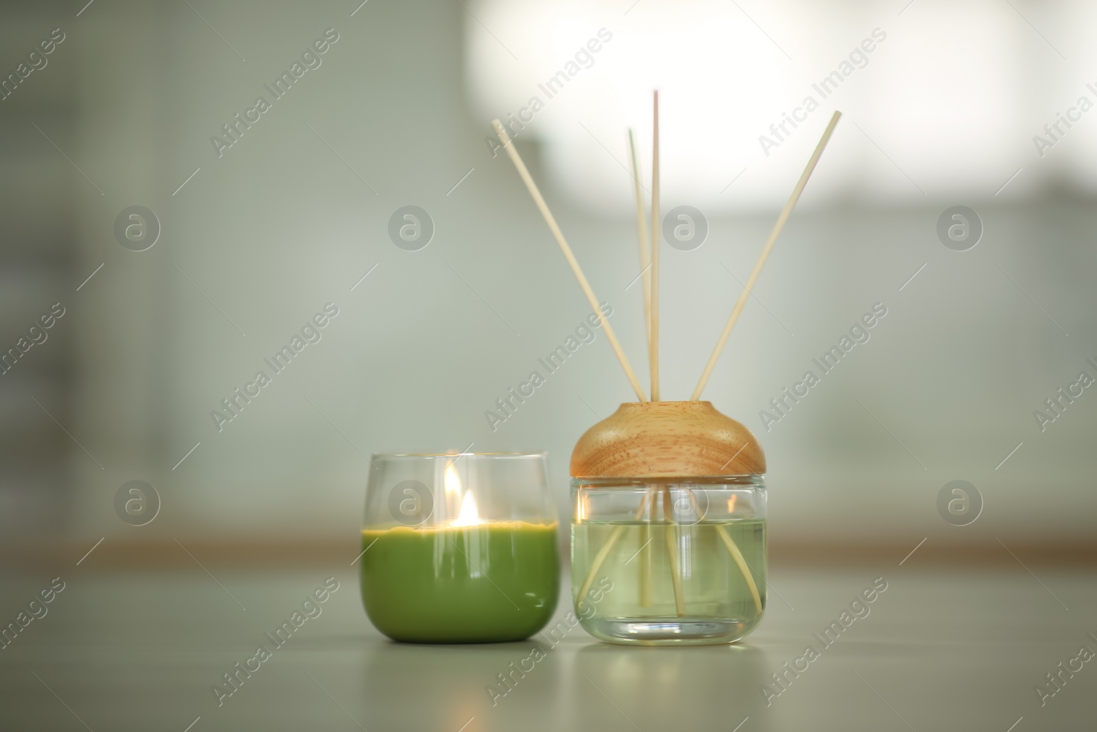 Photo of Aromatic reed air freshener and burning candle on table indoors