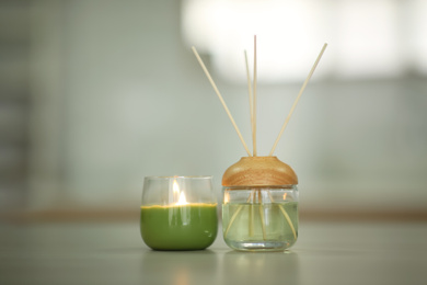Aromatic reed air freshener and burning candle on table indoors