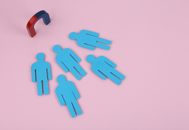 Photo of Magnet attracting paper people on pink background, above view