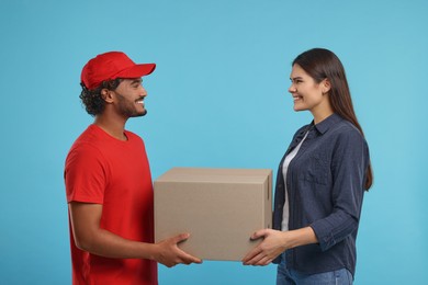 Smiling courier giving parcel to receiver on light blue background