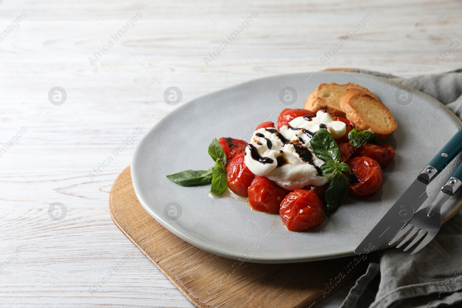 Photo of Delicious burrata cheese served with tomatoes, croutons and basil sauce on white wooden table, space for text