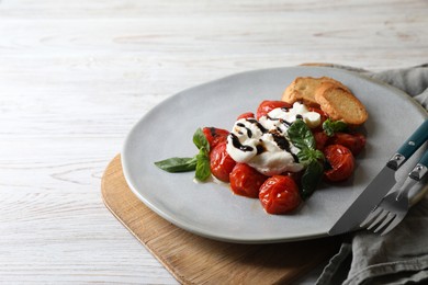 Delicious burrata cheese served with tomatoes, croutons and basil sauce on white wooden table, space for text