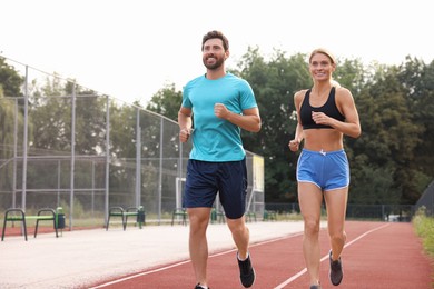 Healthy lifestyle. Happy sporty couple running at stadium, space for text