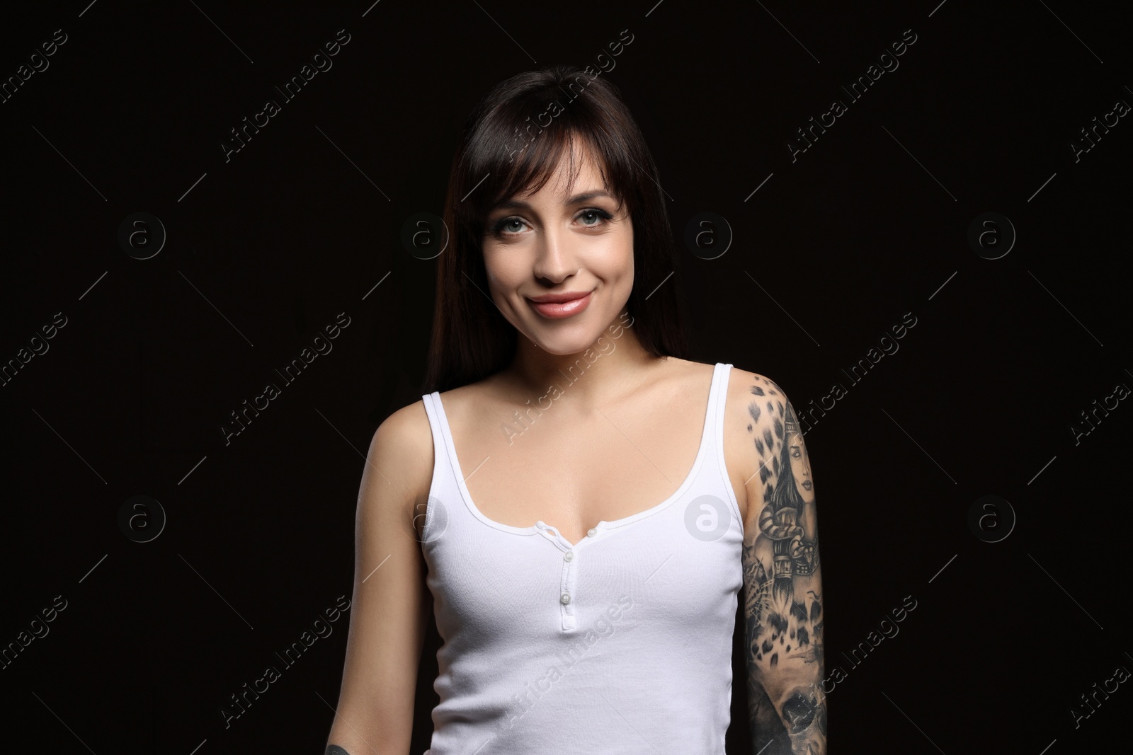 Photo of Beautiful woman with tattoos on arm against black background