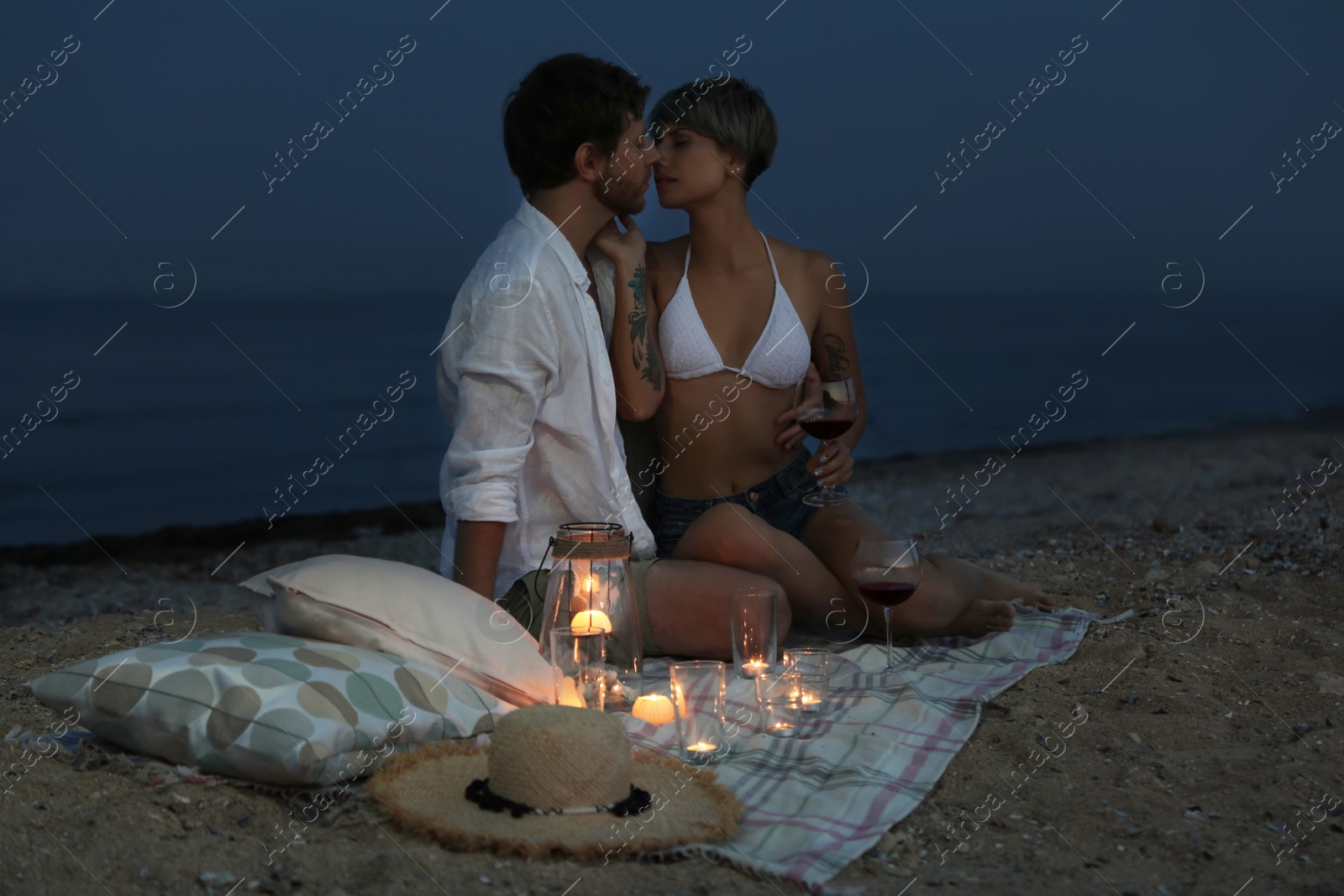 Photo of Young couple with wine and candles on beach