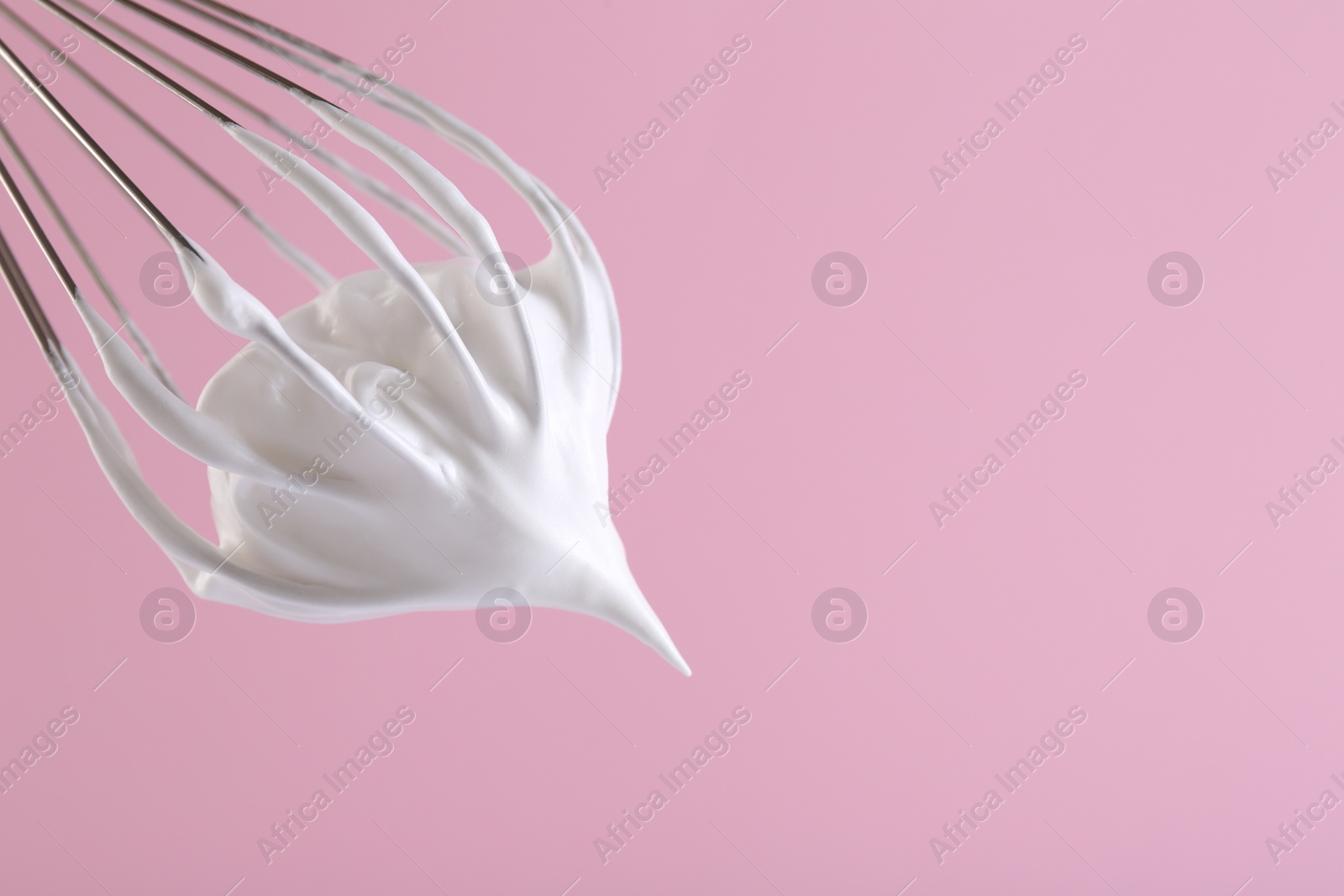 Photo of Whisk with whipped cream on pink background, closeup. Space for text