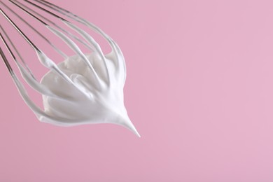 Whisk with whipped cream on pink background, closeup. Space for text