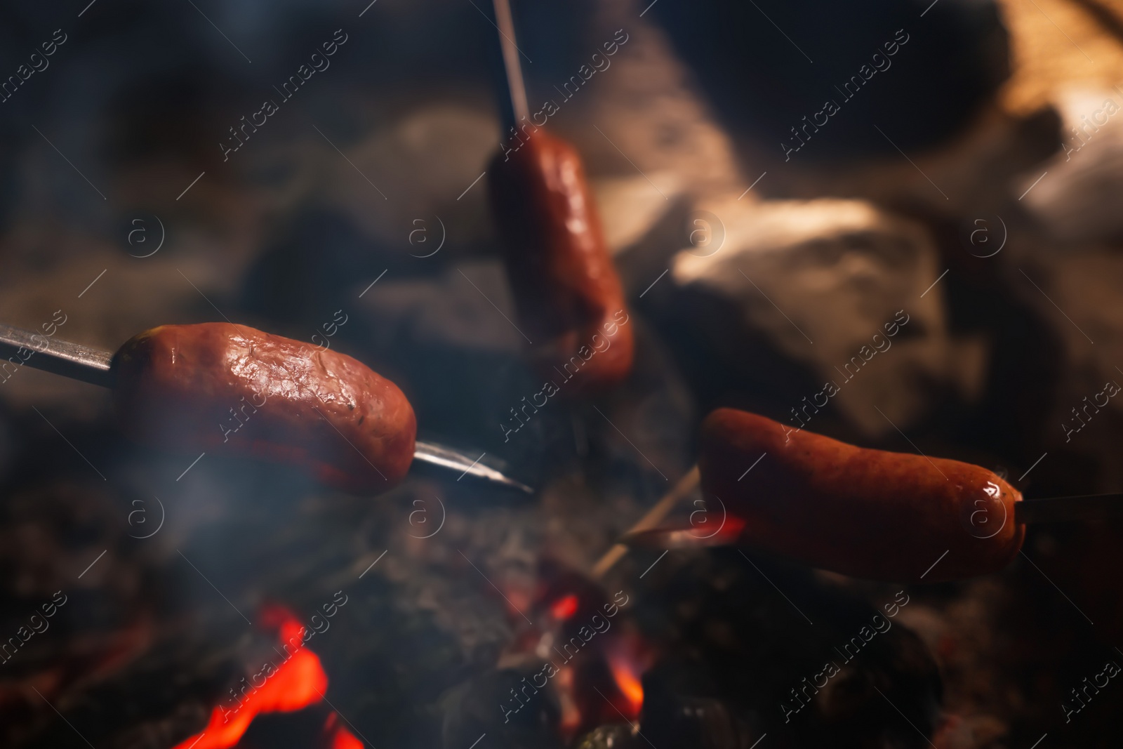 Photo of Roasting sausages on campfire outdoors at night, closeup