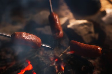 Roasting sausages on campfire outdoors at night, closeup
