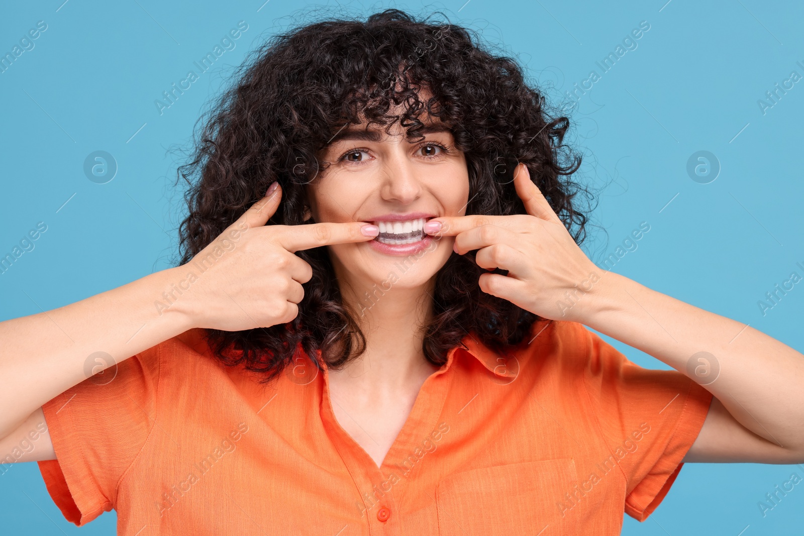 Photo of Young woman applying whitening strip on her teeth against light blue background