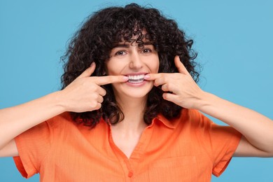 Photo of Young woman applying whitening strip on her teeth against light blue background