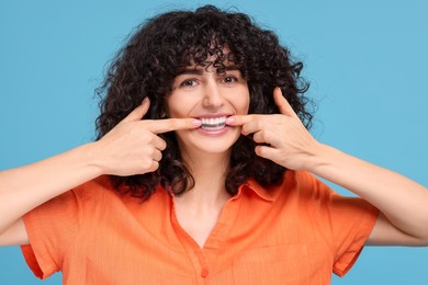 Young woman applying whitening strip on her teeth against light blue background