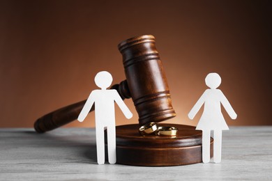 Photo of Divorce concept. Gavel, wedding rings and paper cutout of couple on wooden table