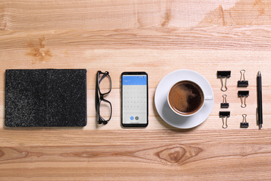 Photo of Flat lay composition of smartphone with calendar app on wooden table