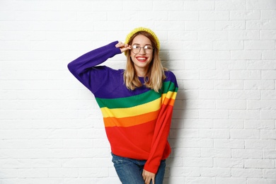 Beautiful young woman in warm sweater with hat near white brick wall