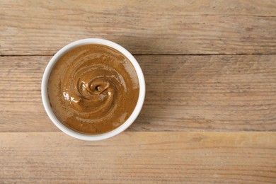 Delicious nut butter in bowl on wooden table, top view. Space for text