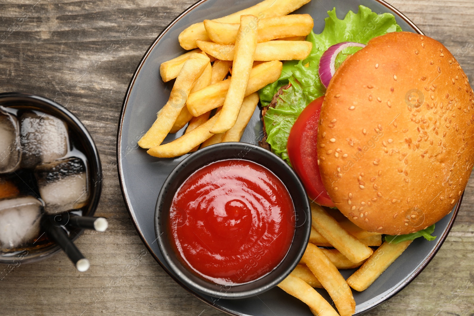 Photo of French fries, tasty burger, sauce and drink on wooden table, flat lay