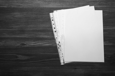 Photo of Punched pockets with paper sheets on black wooden table, flat lay. Space for text