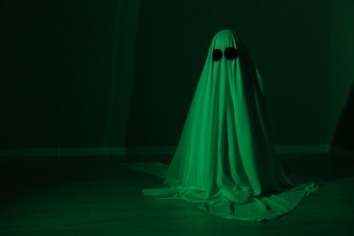 Creepy ghost. Woman covered with sheet in green light, space for text