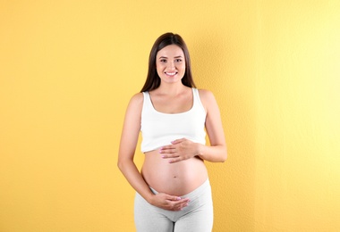 Beautiful pregnant woman holding hands on belly against color background