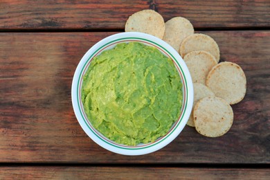 Delicious guacamole made of avocados and nachos on wooden table, flat lay