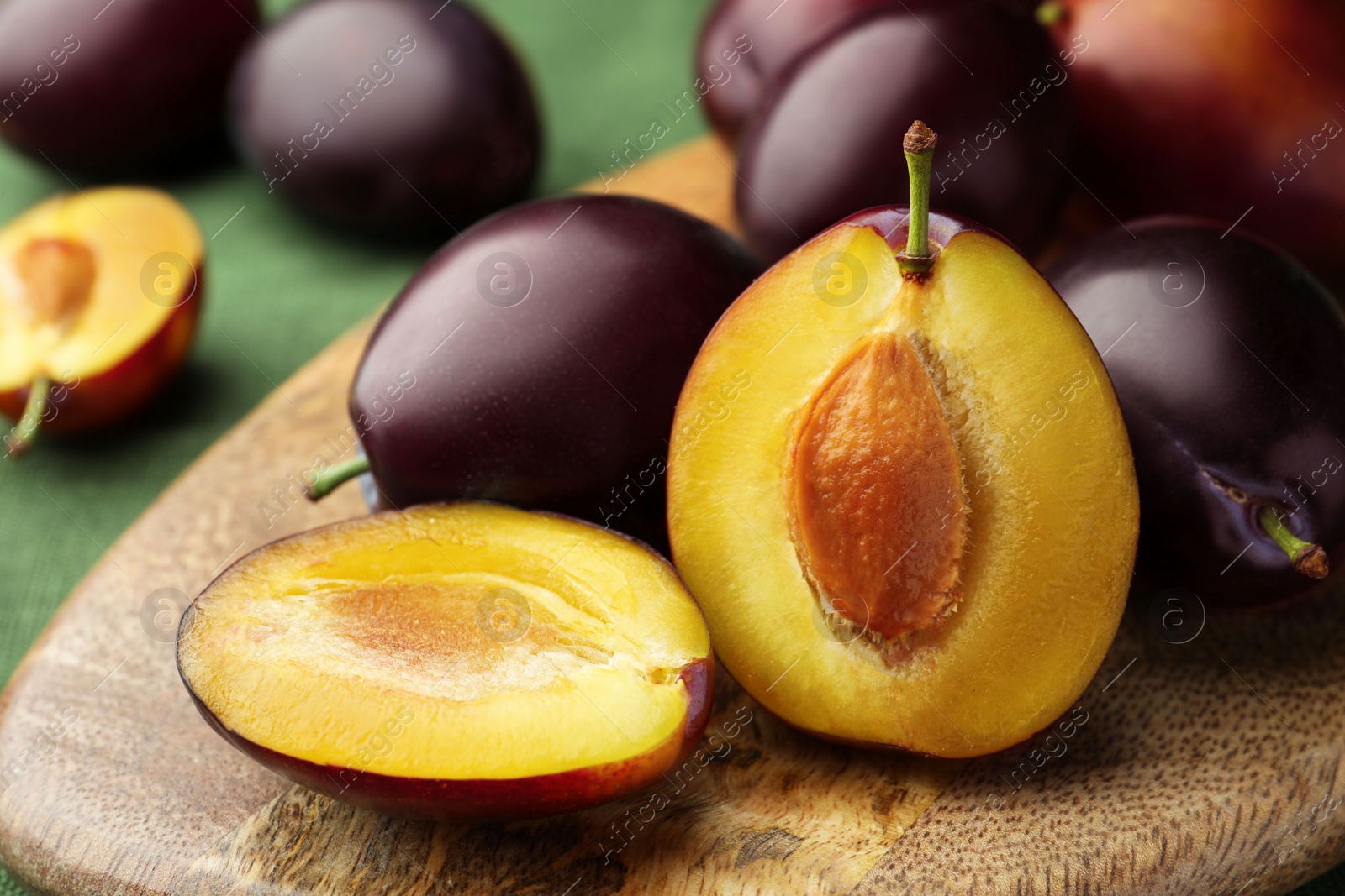 Photo of Many tasty ripe plums on wooden board, closeup