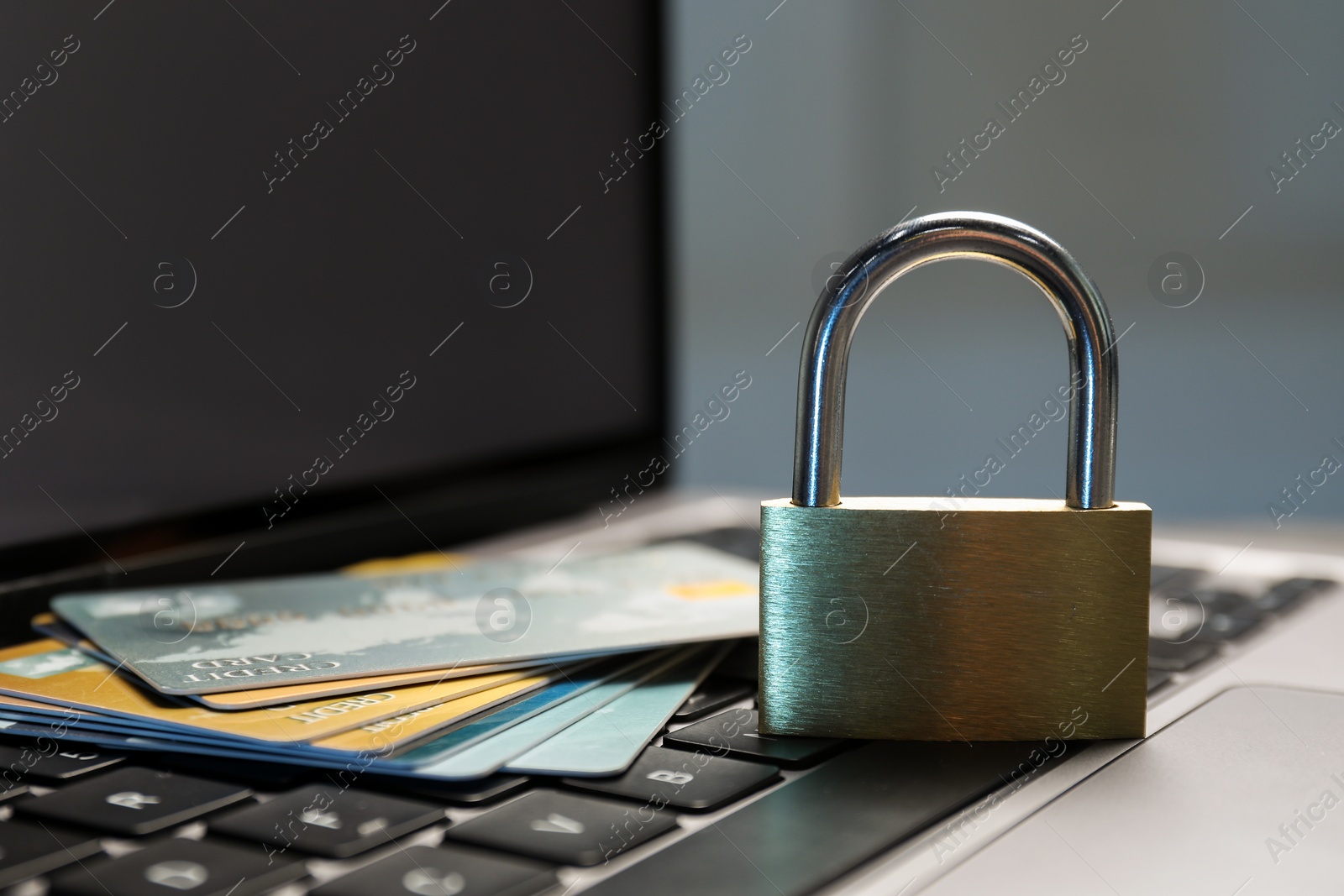 Photo of Cyber security. Metal padlock with chain and credit cards on laptop, closeup