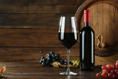 Photo of Winemaking. Tasty wine, barrel and ripe grapes on wooden table, space for text