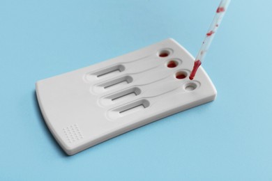 Photo of Dropping blood sample onto disposable express test cassette with pipette on light blue background
