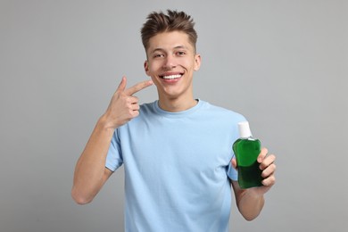 Photo of Young man with mouthwash pointing at his healthy teeth on light grey background