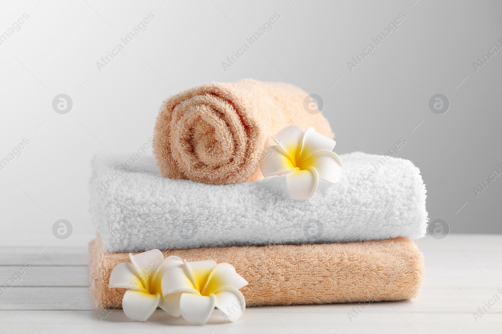 Photo of Soft folded towels and plumeria flowers on white wooden table