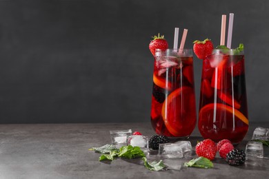 Delicious refreshing sangria, ice cubes and berries on grey table, space for text