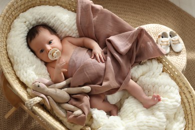 Cute newborn baby with pacifier and toy bunny lying in cradle at home, top view