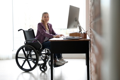 Woman in wheelchair working with computer at table indoors