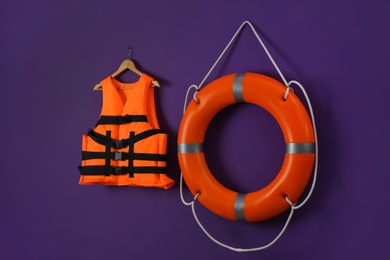 Photo of Orange life jacket and lifebuoy on violet background. Rescue equipment