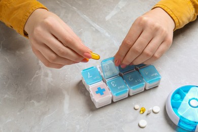 Woman putting pill into plastic box at grey marble table, closeup