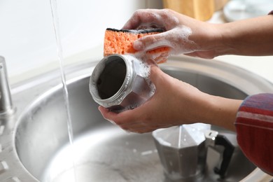 Photo of Woman washing moka pot (coffee maker) above sink in kitchen, closeup