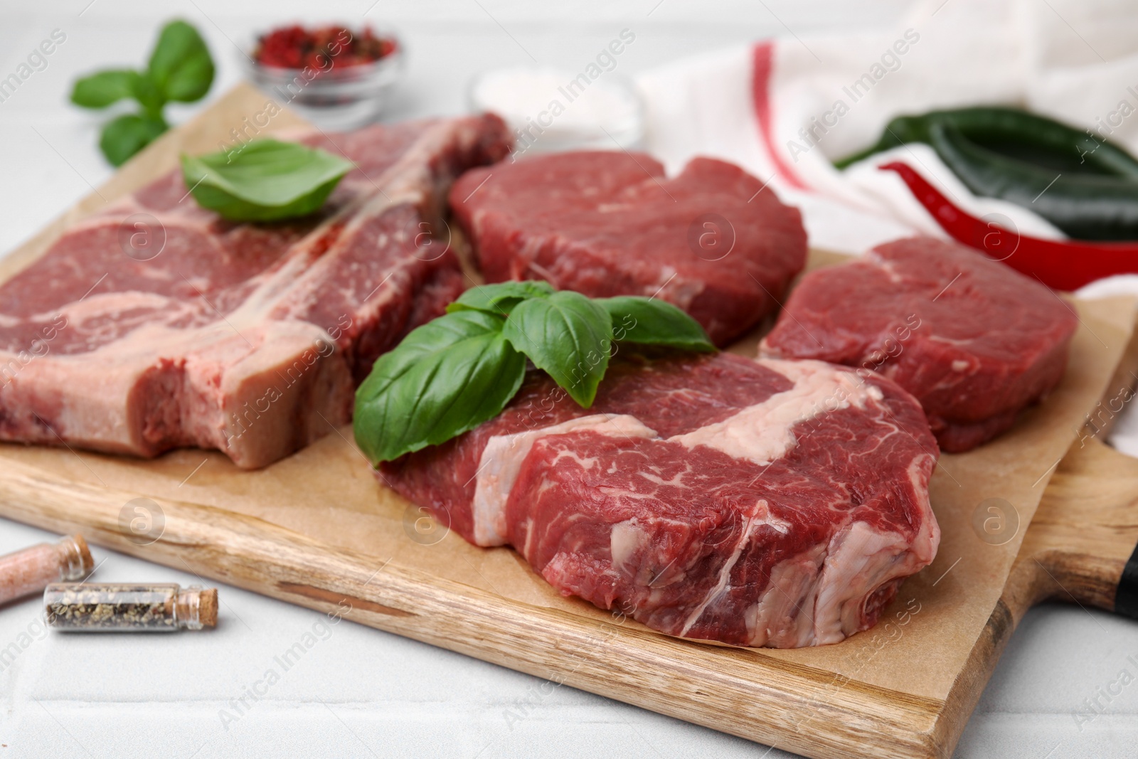 Photo of Cut fresh beef meat and basil leaves on white table, closeup