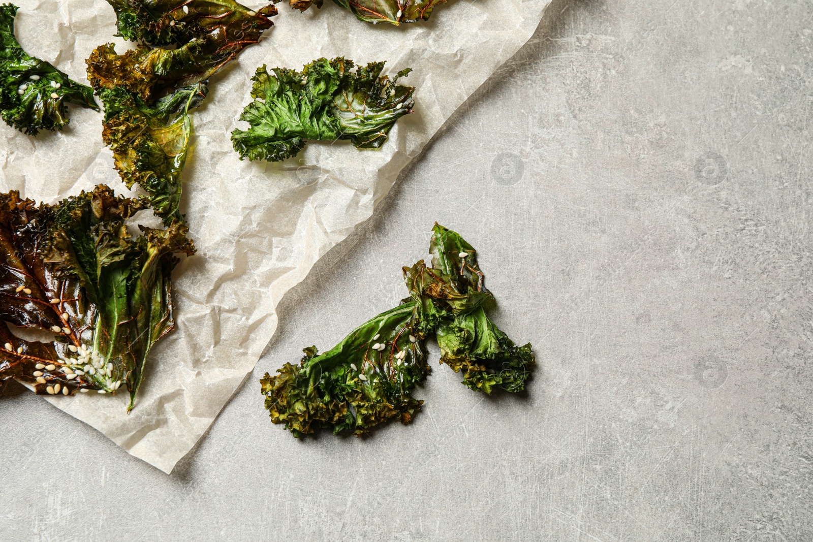 Photo of Tasty baked kale chips on grey table, flat lay