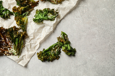 Tasty baked kale chips on grey table, flat lay