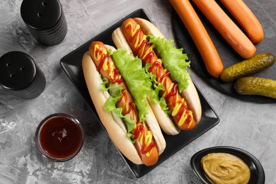 Tasty hot dogs and ingredients on grey textured table, flat lay