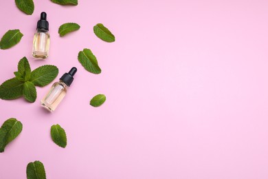 Bottles of essential oil and mint on pink background, flat lay. Space for text