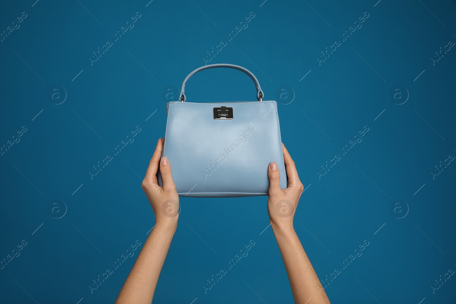 Photo of Woman holding stylish handbag on blue background, closeup