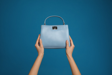 Woman holding stylish handbag on blue background, closeup