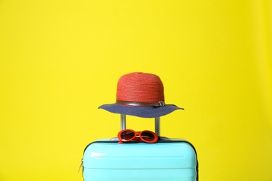 Stylish blue suitcase with hat and sunglasses on yellow background