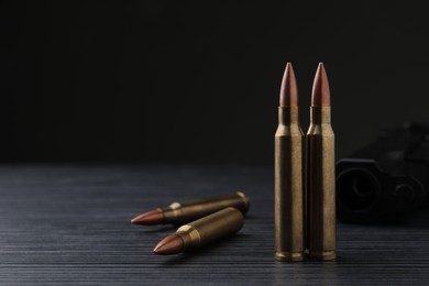 Photo of Bullets and pistol on black wooden table. Space for text