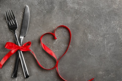 Photo of Cutlery set and red ribbon on grey background, flat lay with space for text. Valentine's Day dinner