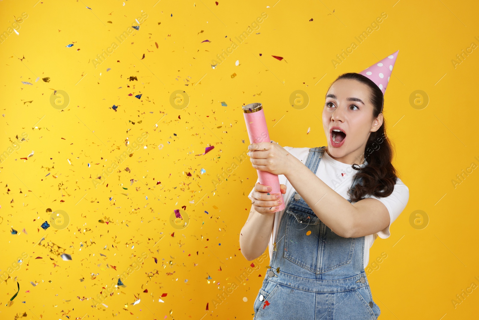 Photo of Young woman blowing up party popper on yellow background